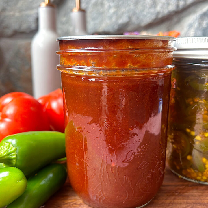 a jar of homemade bbq sauce with jalapenos and tomatoes on the side
