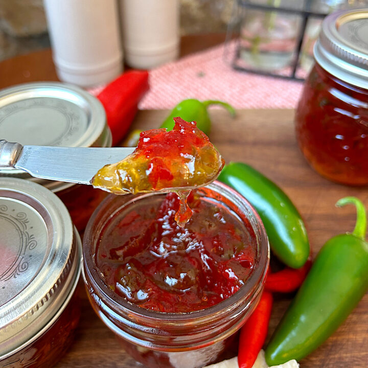a jar of pepper jelly on a wood board with cheese and crackers