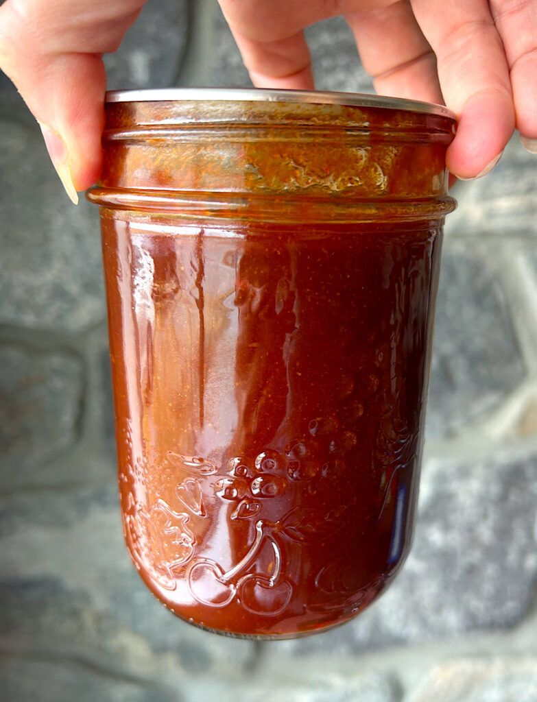a pint jar of homemade bbq sauce in front of a stone wall