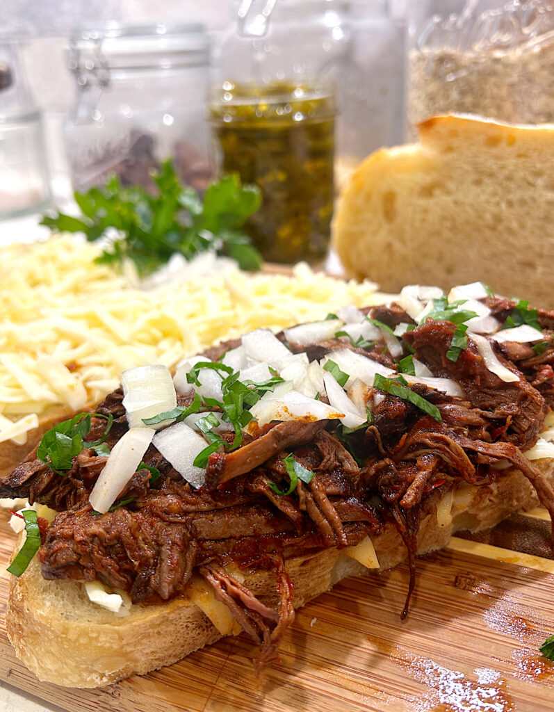 a slice of bread topped with cheese, shredded meat, onion and cilantro