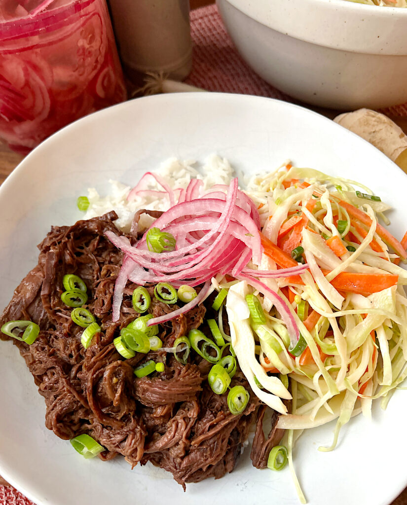 a white bowl with rice, cabbage slaw, shredded venison and pickled onions