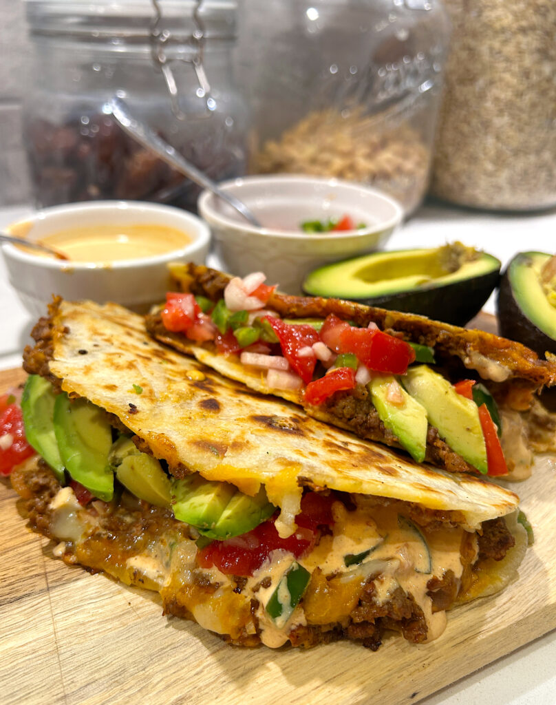 two venison and cheese tacos on a wood board with salsa and avocado