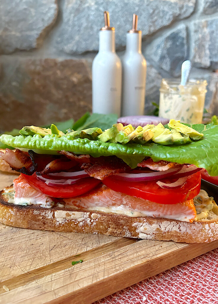 a slice of bread topped with salmon, lettuce, tomato, bacon and avocado