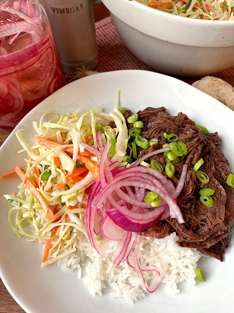 a white bowl with rice and shredded venison roast topped with pickled onions and cabbage
