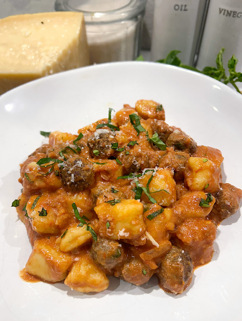 a white bowl of gnocchi with meatballs in a tomato basil sauce