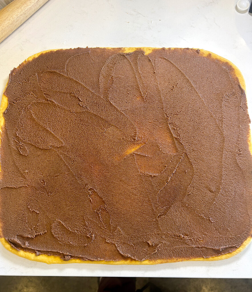 a rectangle of dough on a white counter with cinnamon sugar filling on top