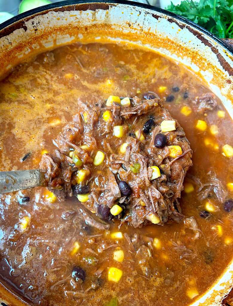 a large pot of tomato soup full of shredded meat, corn and black beans