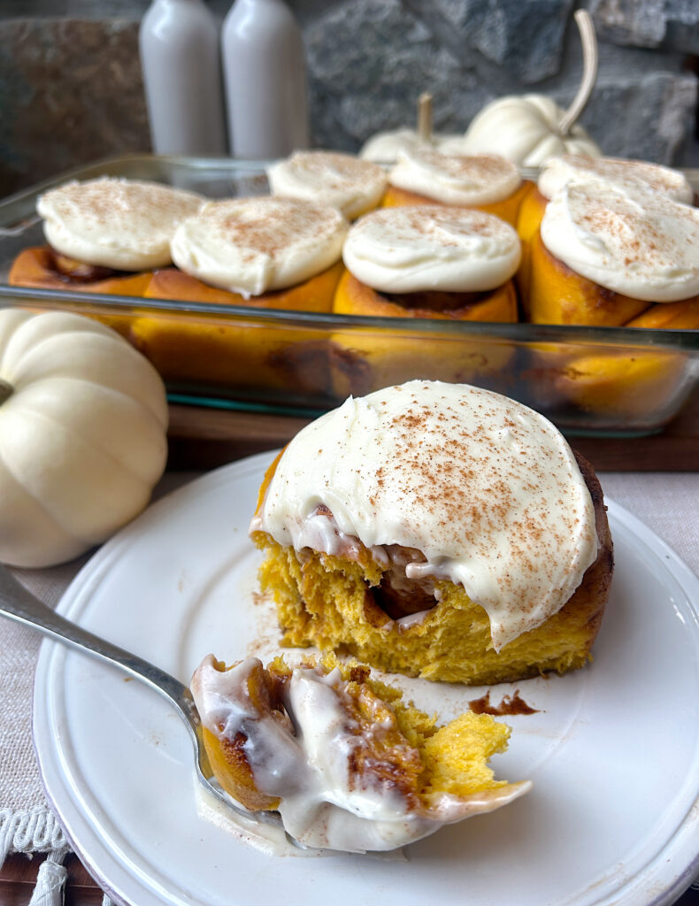 a white plate with a pumpkin cinnamon bun with cream cheese icing