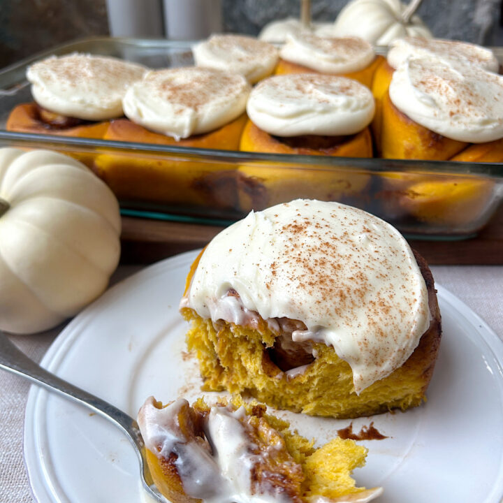 a white plate with a pumpkin cinnamon bun with cream cheese icing