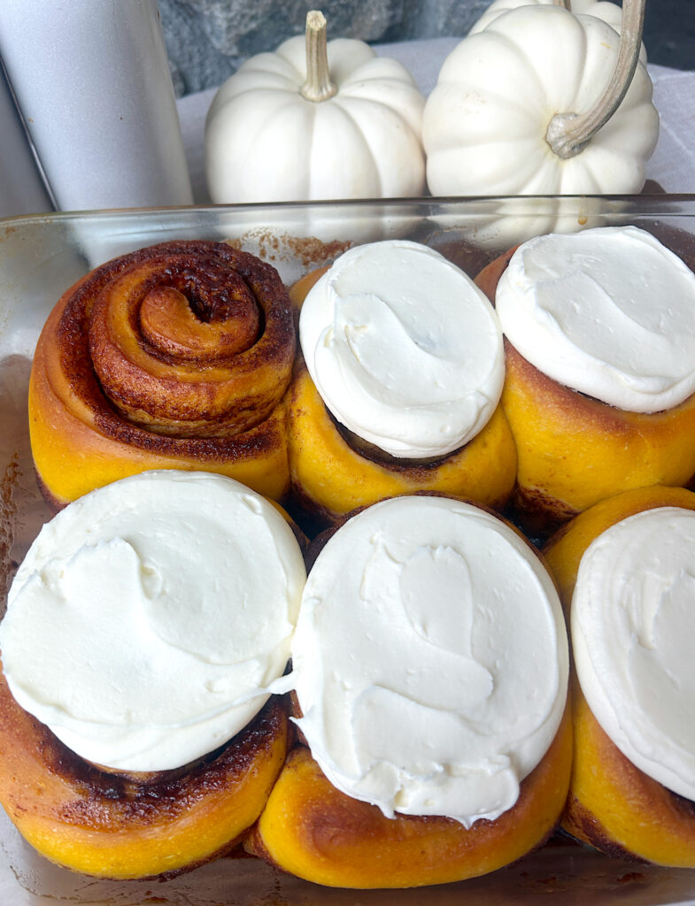 a baking dish full of pumpkin cinnamon buns with cream cheese frosting