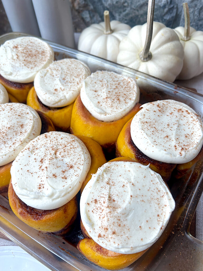 pumpkin cinnamon buns in a baking dish topped with cream cheese frosting