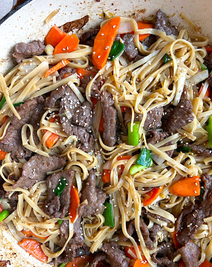 a skillet of noodles with vegetables and think sliced venison