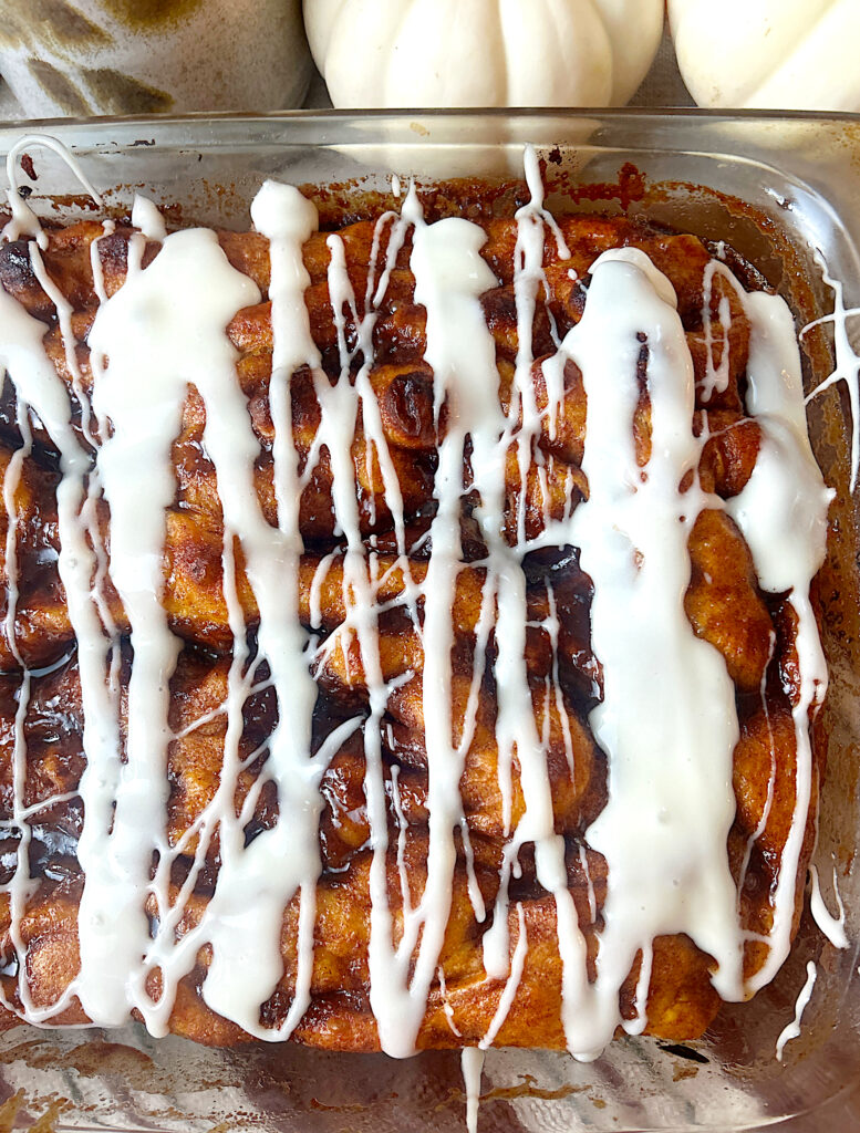 a tray of pumpkin focaccia bread with a cinnamon swirl and cream cheese glaze on top