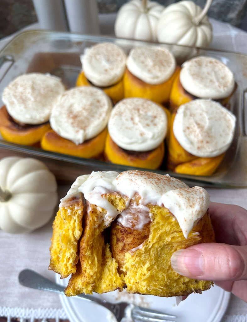 a pumpkin sourdough cinnamon bun with cream cheese frosting with a bite taken out of it