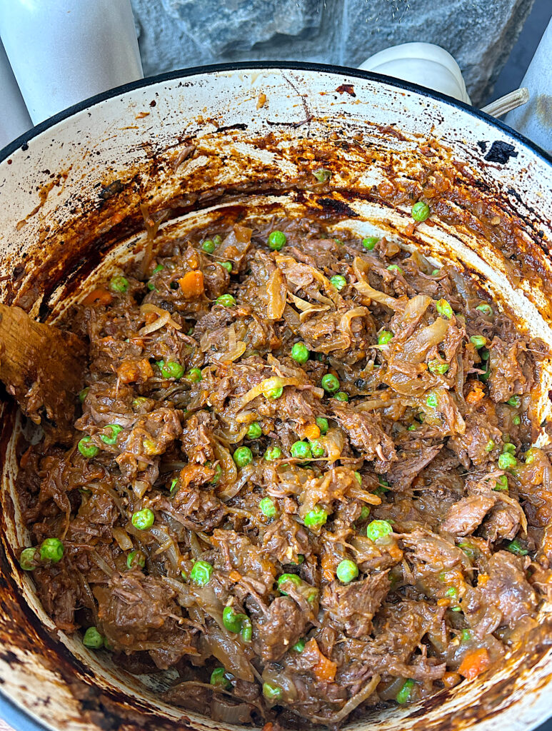 a dutch oven of slow braised meat with carrots, peas and onions