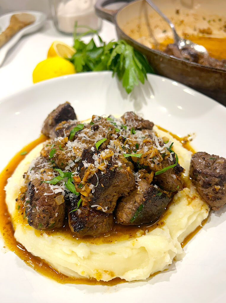 a white bowl with mashed potatoes and venison steak bites on top