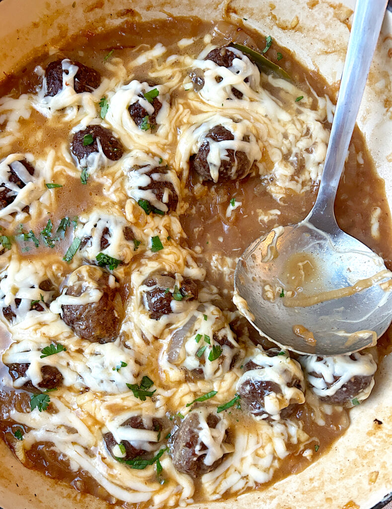 a skillet of meatballs in French onion sauce with cheese on top