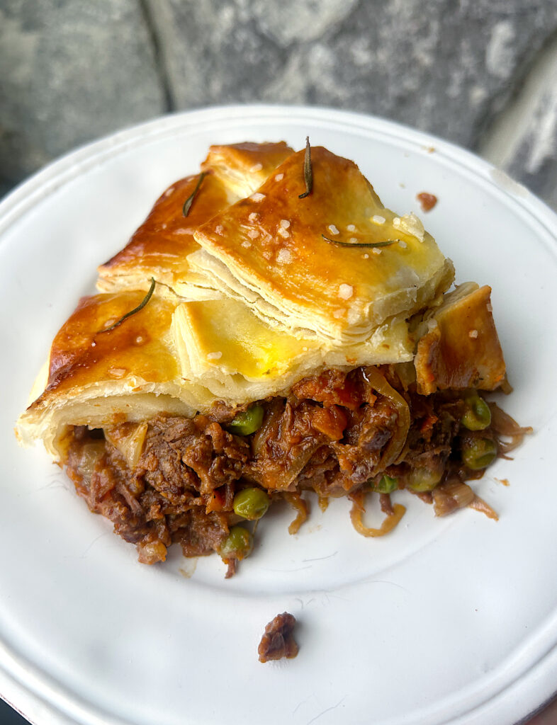 a slice of venison pot pie with golden brown puff pastry on a white plate