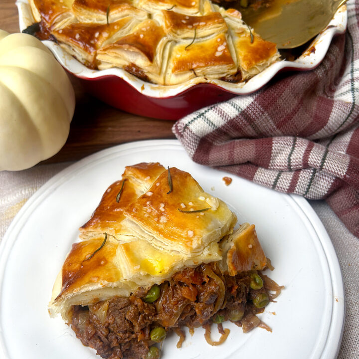 a white plate with a slice of meat pie with flaky pastry on top