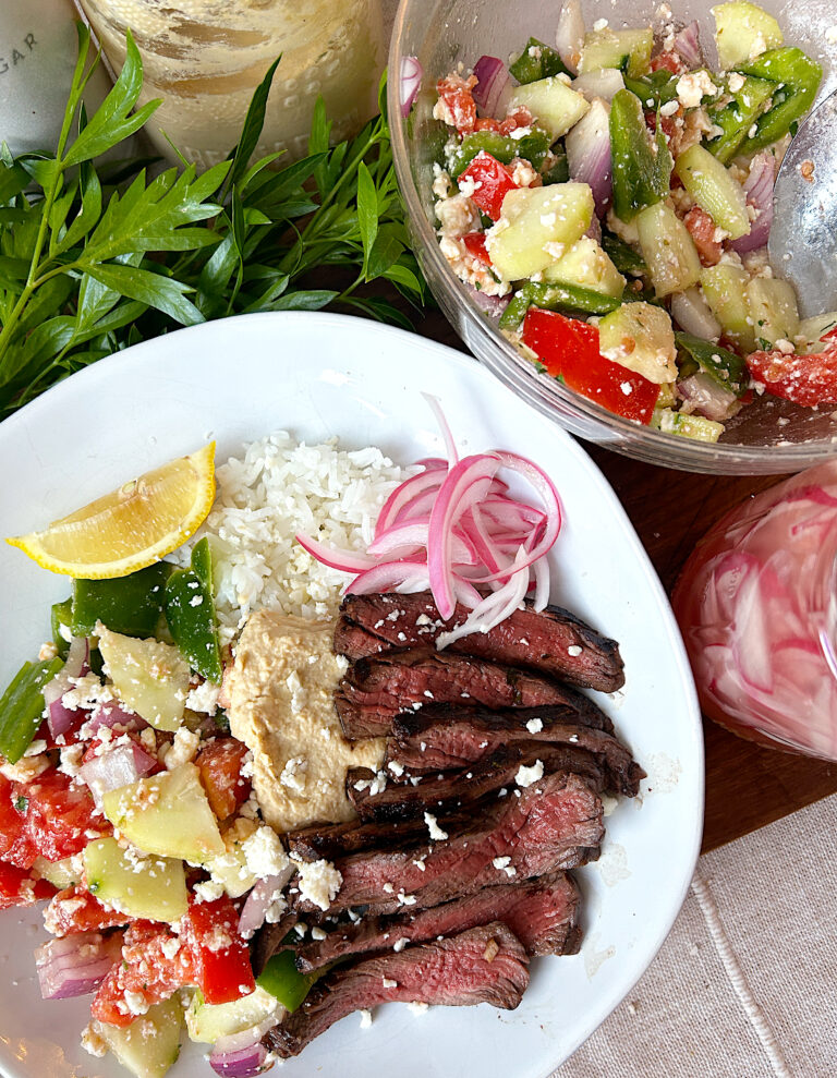 a bowl of rice, greek salad, hummus, pickled onions and sliced steak