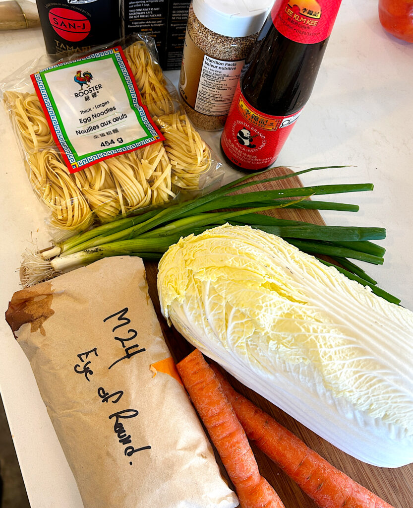 egg noodles, cabbage, carrots, green onions and a round roast on a white counter