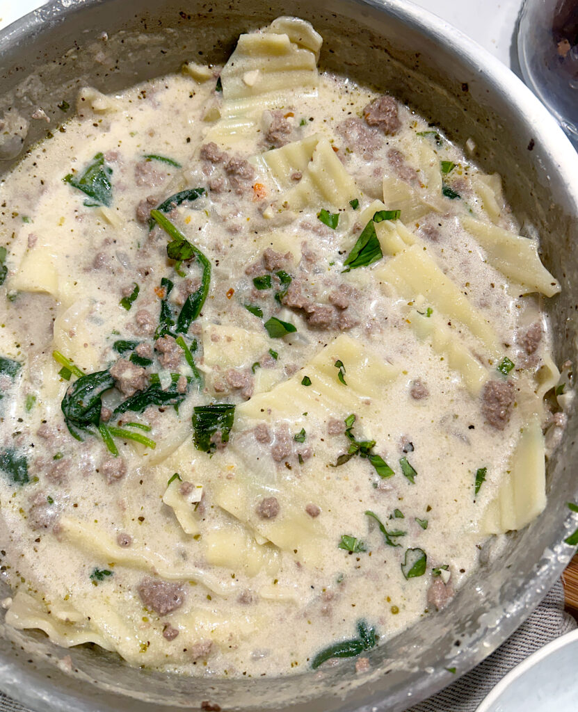 a large stainless steel pot of cream soup with lasagna noodles, spinach and ground meat
