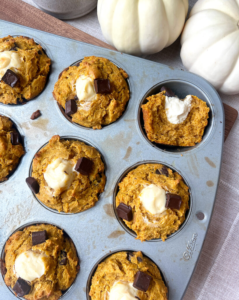a muffin tray of pumpkin muffins with a cream cheese centre