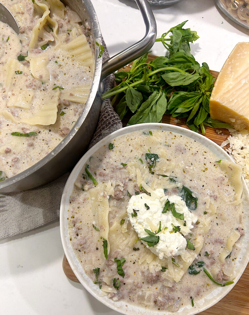 a bowl of creamy soup with noodles, meat, and fresh basil