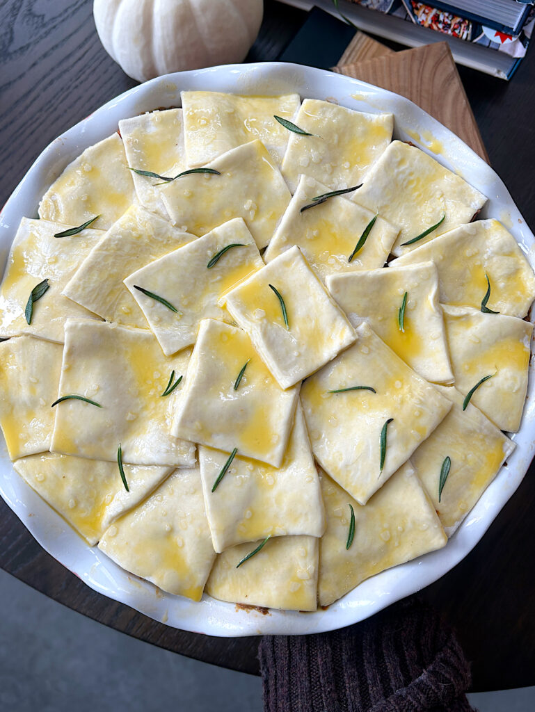 an unbaked meat pie topped with squares of puff pastry and egg wash