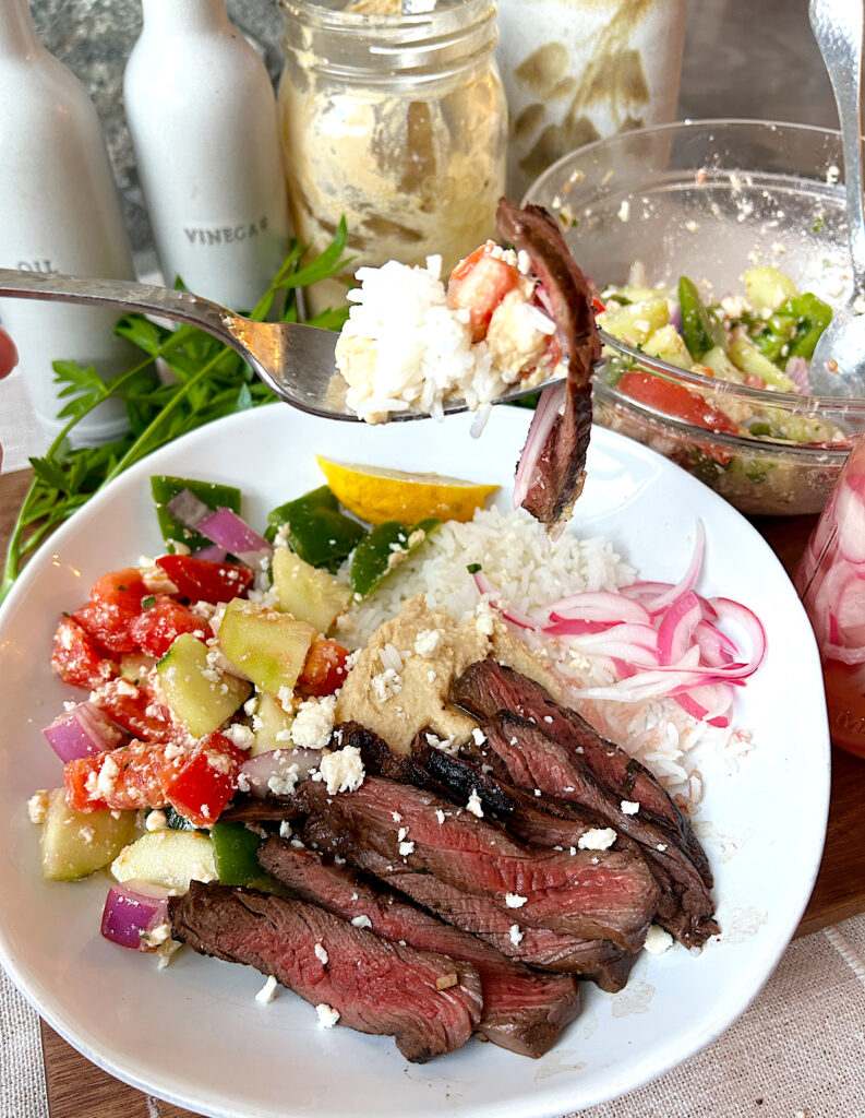 a rice bowls topped with greek salad, and sliced venison steak