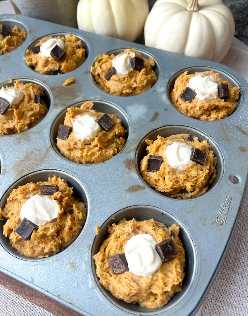 a tray of unbaked muffins filled with cream cheese and chocolate chunks