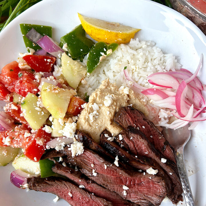 a white bowl of rice, greek salad, venison steak and hummus