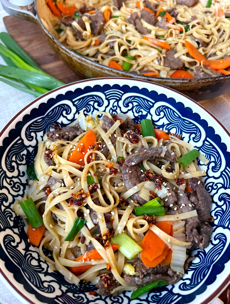 a blue and white bowl of noodle stir fry with vegetables and sliced venison