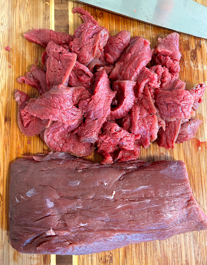 a venison roast sliced thin into strips on a wood board