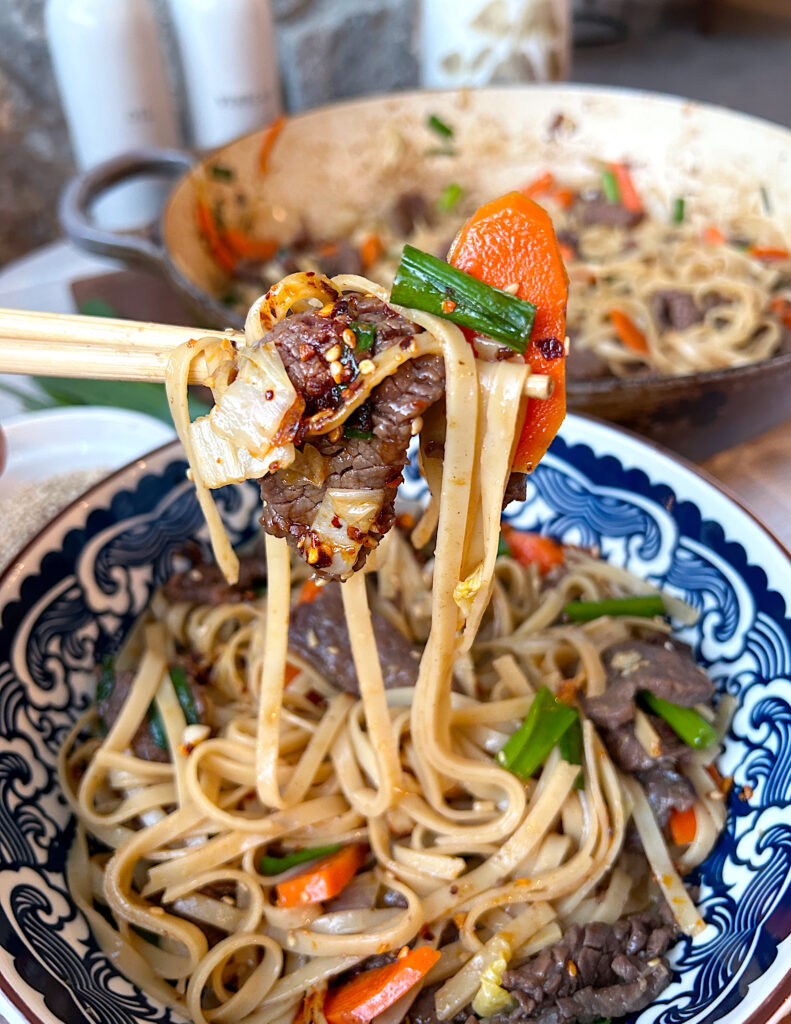 chopsticks with a bite of noodles, vegetables and meat