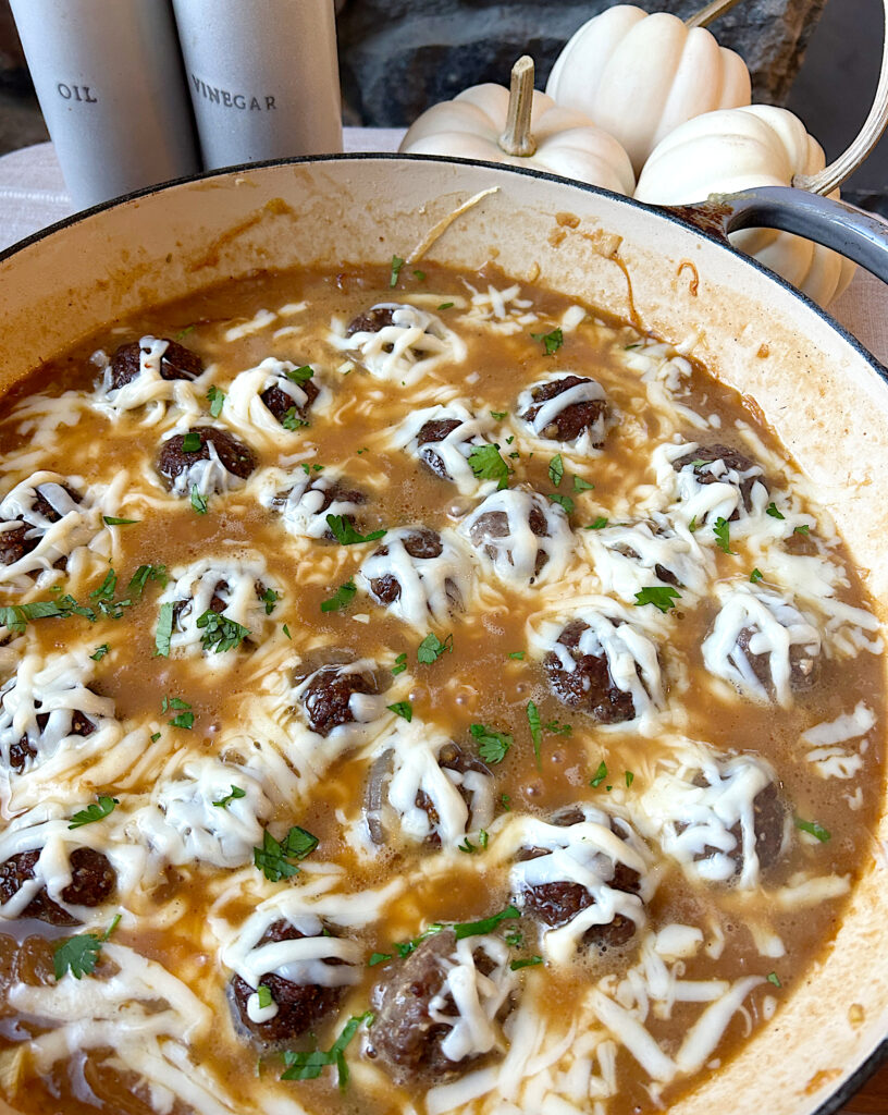 a skillet of meatballs in lads of caramelized onions topped with melted cheese