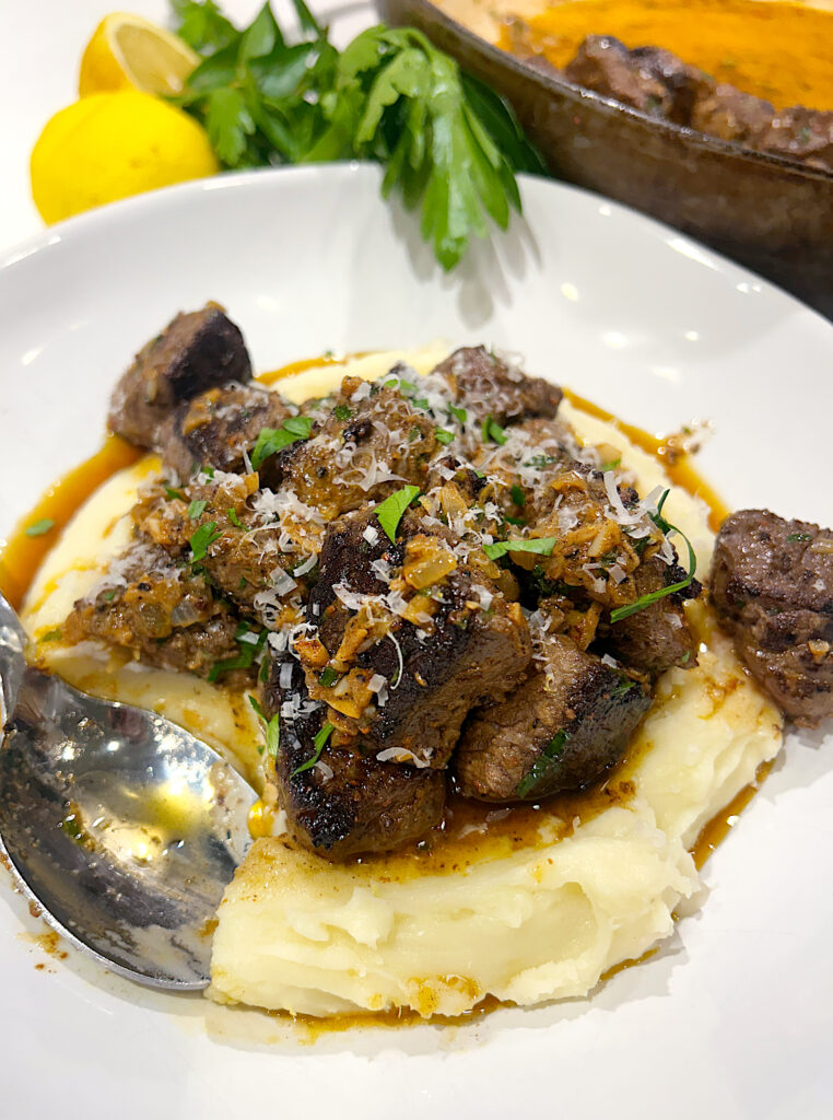 a white bowl with mashed potatoes and steak bites on top
